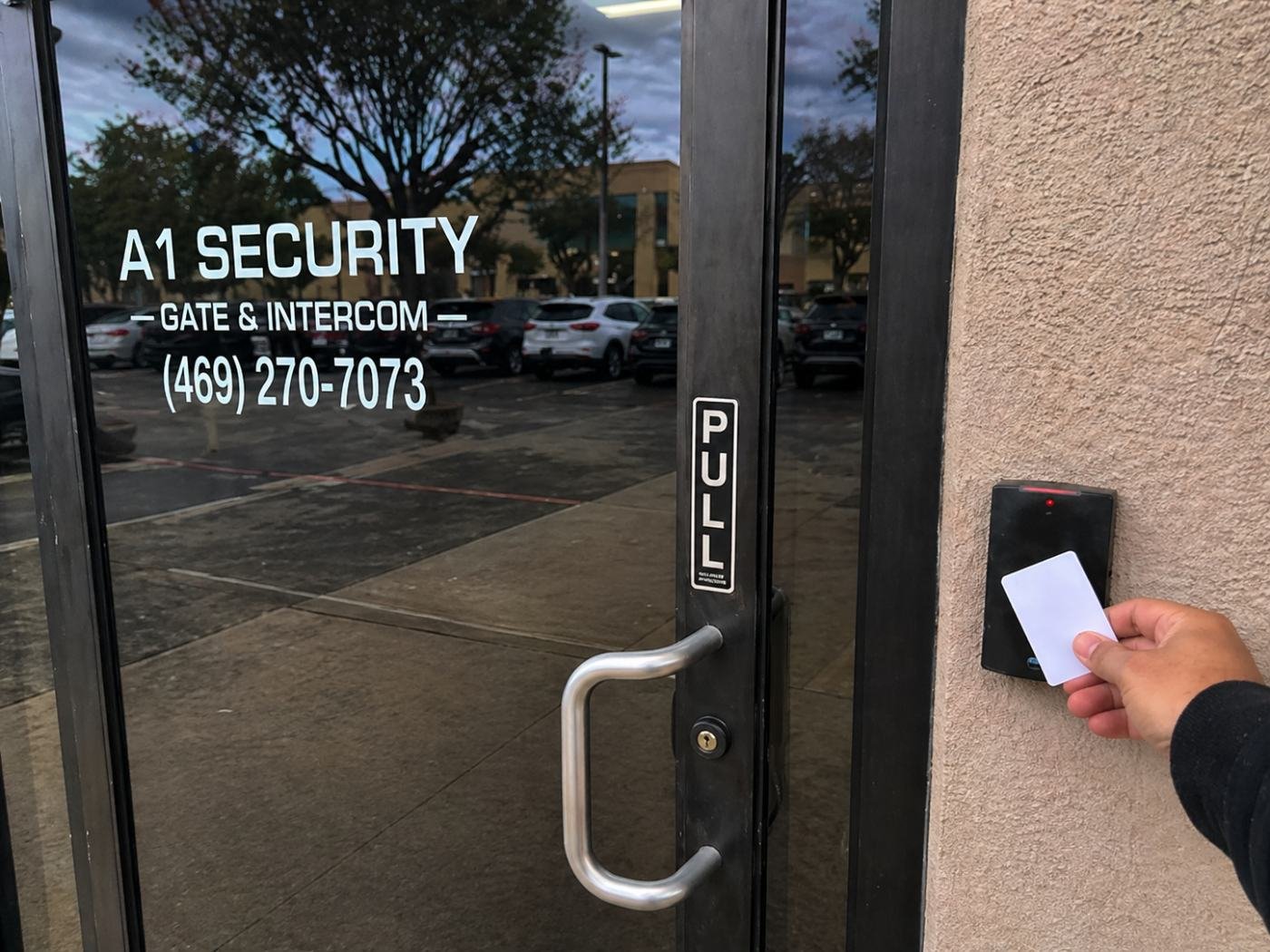 Hand presenting a proximity access card to a wall-mounted reader at a commercial office entrance in Dallas