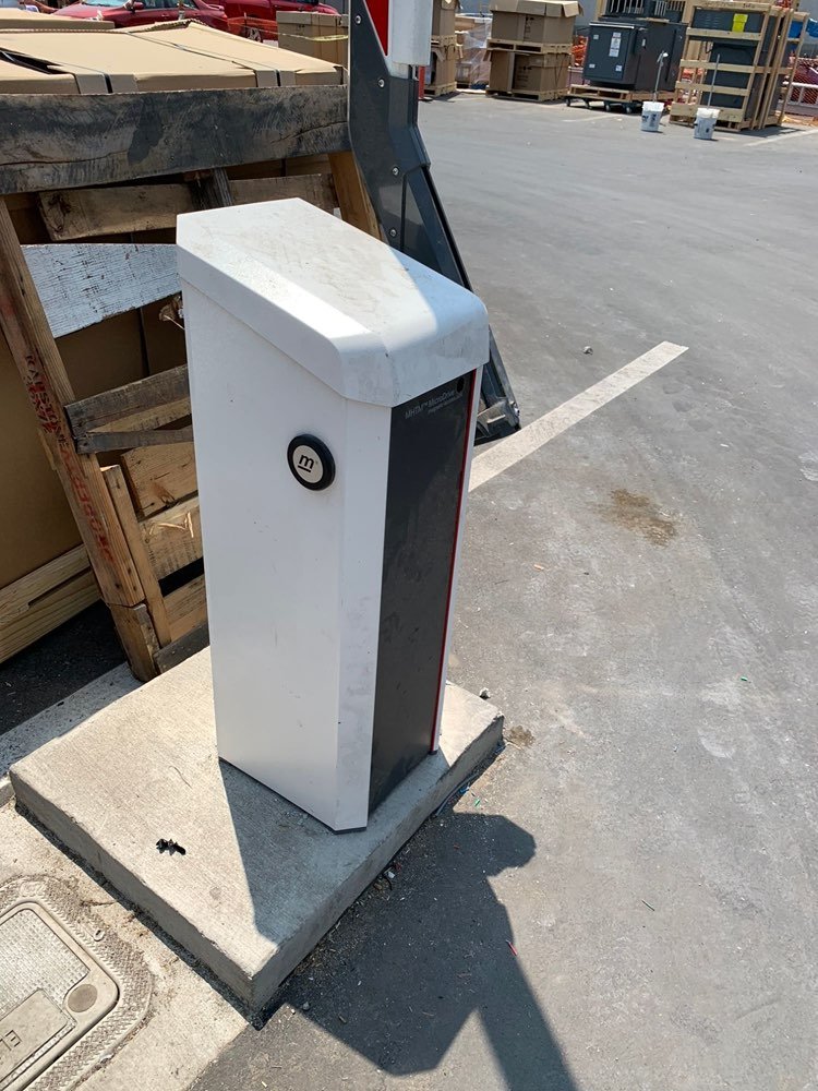 Barrier arm gate operator mounted on a concrete pad at a commercial lot in DFW