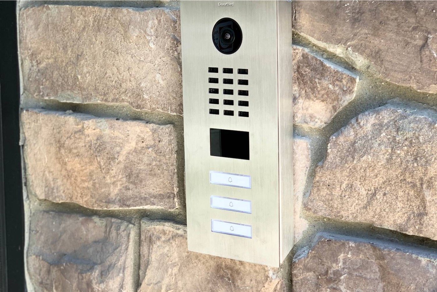 Stainless steel video intercom with camera, keypad and resident call buttons mounted on a stone entry wall